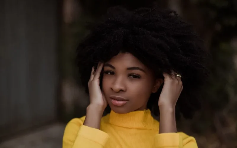 Young dreamy African American black haired female touching curly hair while standing on street