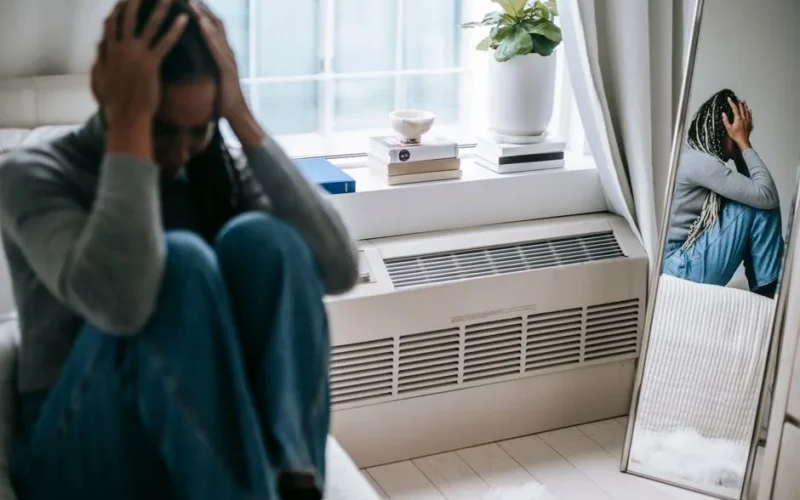 Frustrated young female having mental problem reflecting in mirror while sitting alone in room