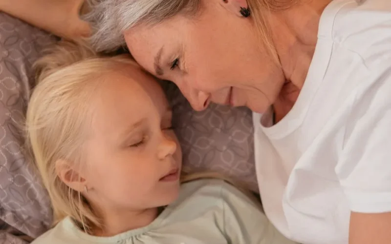 Grandmother and granddaughter sharing a tender, loving moment while lying close together indoors.