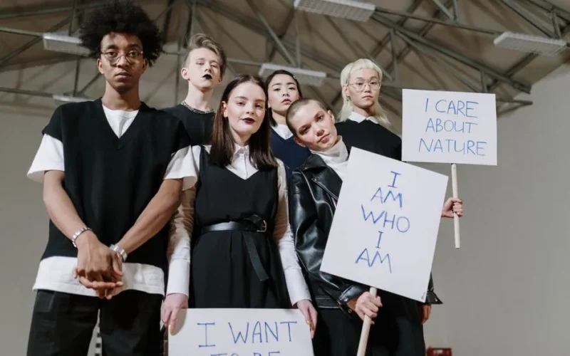 A diverse group of teenagers holding protest signs indoors, advocating individuality and environmental care.
