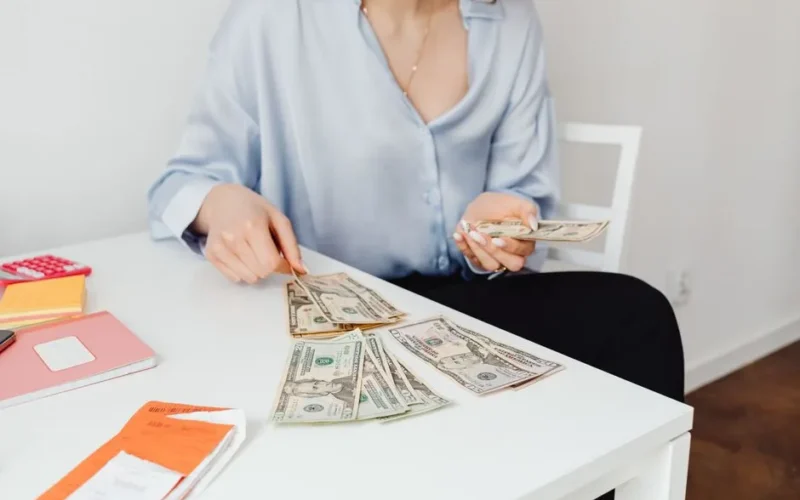 A woman counts US dollar bills at a desk, symbolizing finance management.
