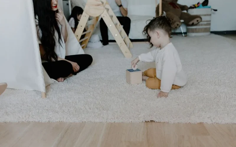 A mother and child enjoying playtime on a carpeted floor with toys.
