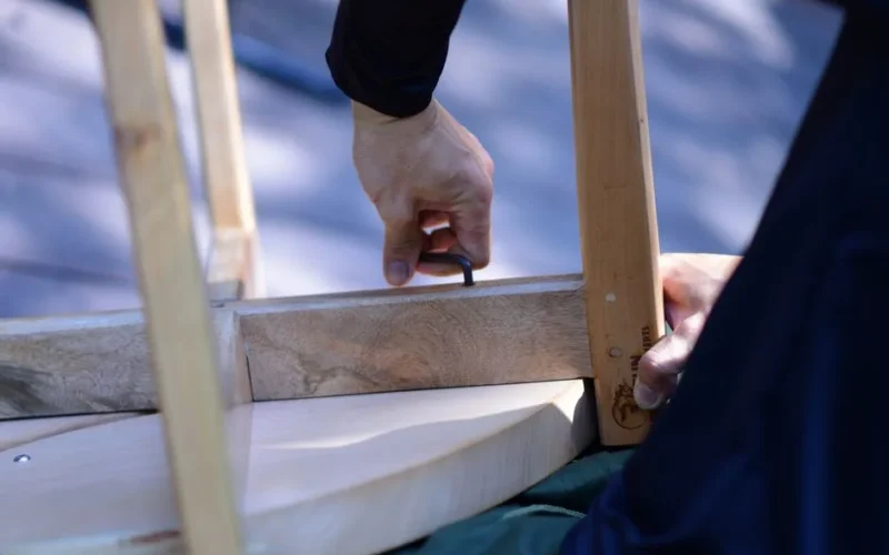 Close-up of a person assembling wooden furniture with an Allen wrench on a sunny day.