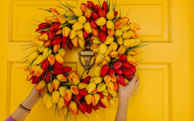 Colorful tulip wreath held by hands on a yellow door, perfect for spring decor.