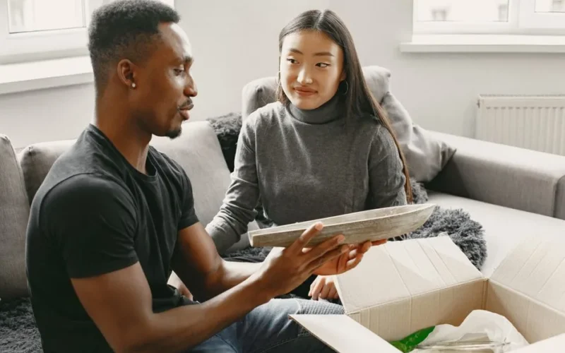 A happy interracial couple unboxing a package together at home while sitting on a couch.