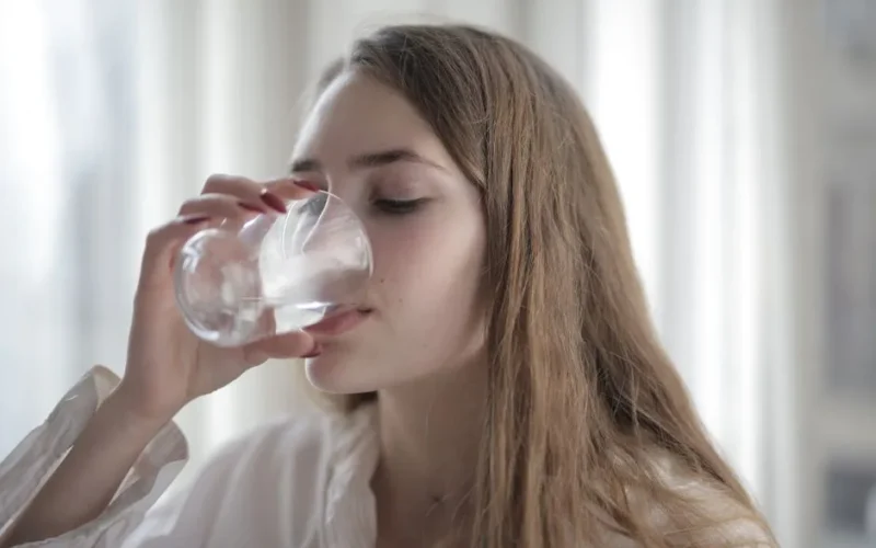 A woman enjoying a refreshing glass of water indoors during the day.