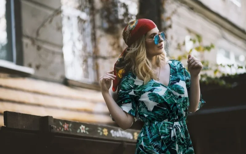 Fashionable woman wearing tropical dress and headscarf, posing outdoors in urban setting.