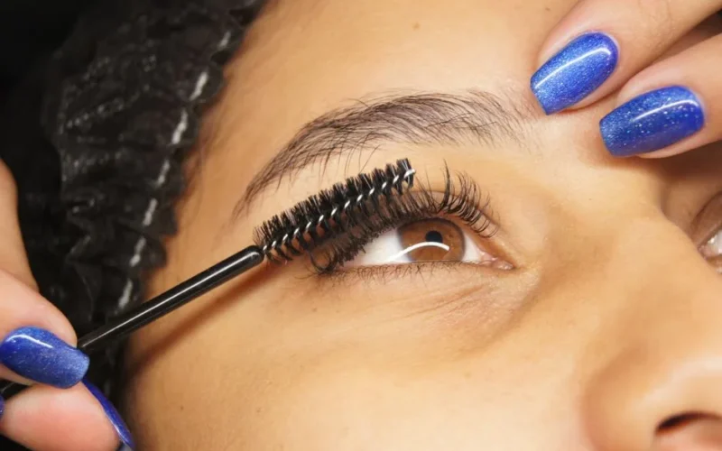 Detailed shot of eyelash extension application on a woman with blue painted nails.