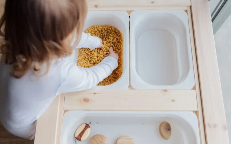 Curious child engaging in sensory play with pasta, exploring textures indoors.