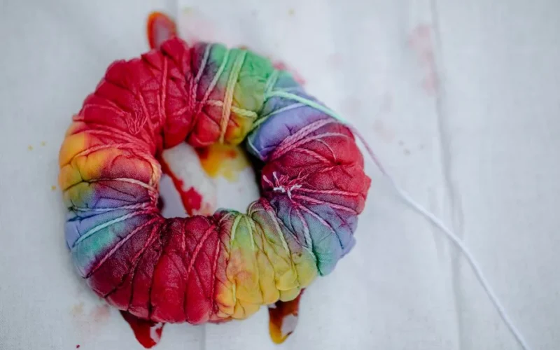 Top view of pleated textile with multicolored paints tied with threads representing Japanese tie dye technique