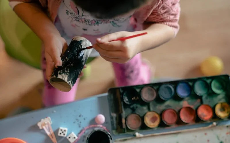 Top view of a child painting a cardboard roll with watercolors, showcasing creativity and art.