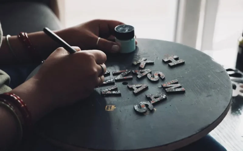 Hands painting letters on a circular board for crafting or design project.