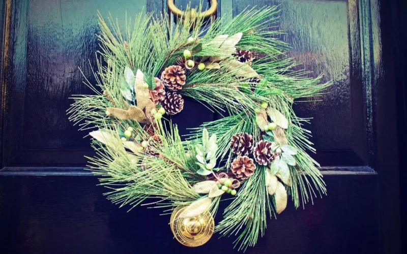 Elegant Christmas wreath with pinecones and greenery on a dark wooden door, adding festive charm.