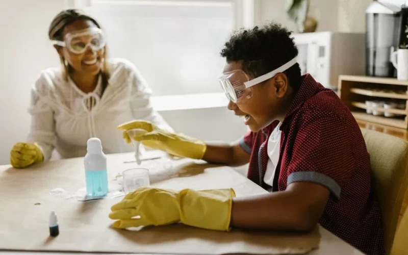 Boy and woman conducting a science experiment at home, wearing gloves and goggles.