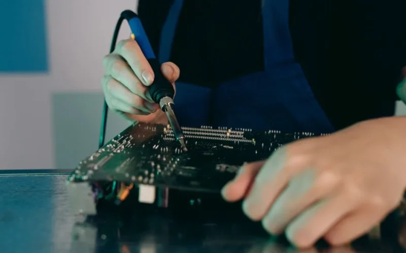 Close-up view of hands soldering electronic components on a circuit board.