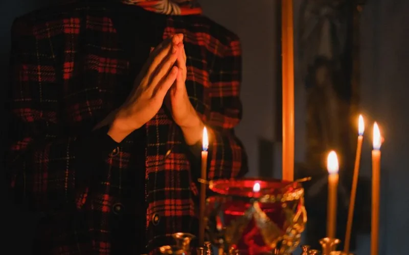 A person praying with candles in a dark, spiritual church setting.