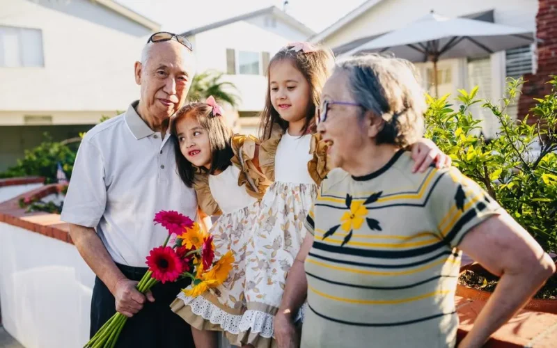 Asian grandparents with twin grandchildren enjoying a sunny day outdoors with flowers.