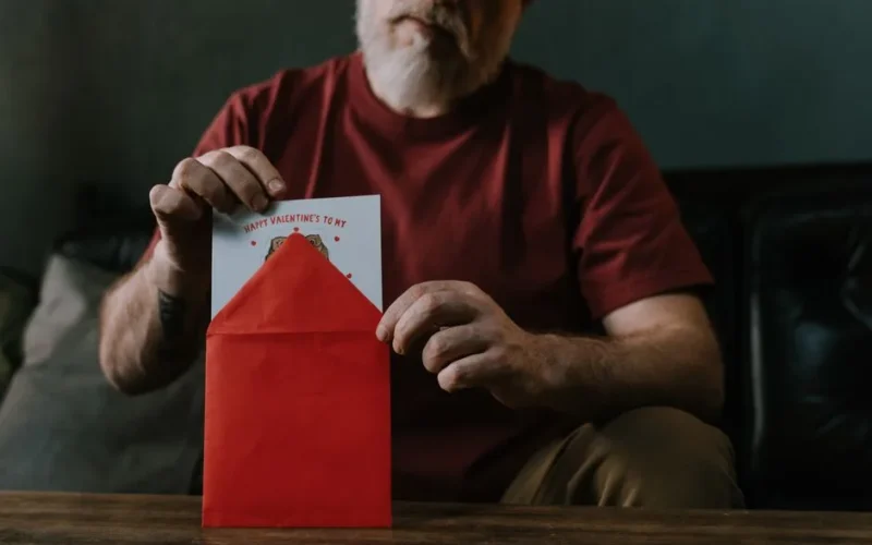 An elderly man opening a red envelope containing a Valentine's Day card, symbolizing love and connection.