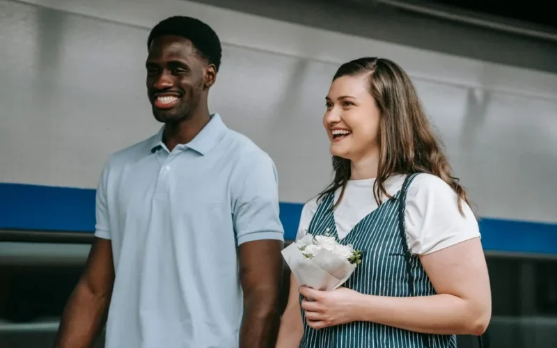 A cheerful interracial couple holding flowers, captured indoors, showcasing love and joy.