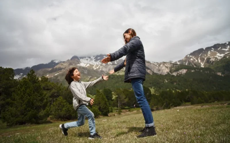 A mother and child embrace joyfully in a lush mountain setting, capturing a moment of happiness and love.