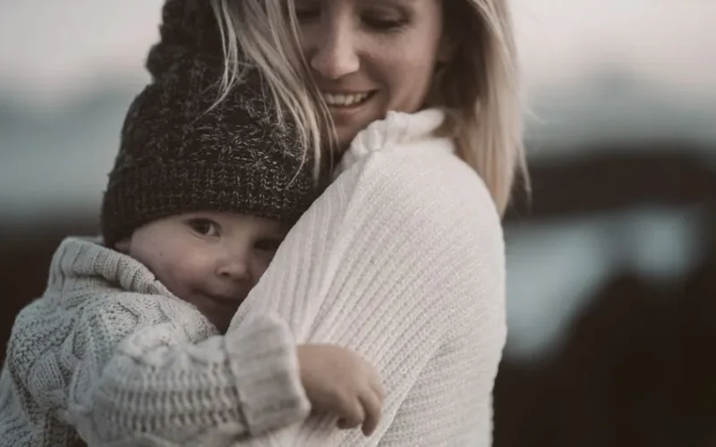 A tender moment of a mother embracing her child in cozy knitwear outdoors.