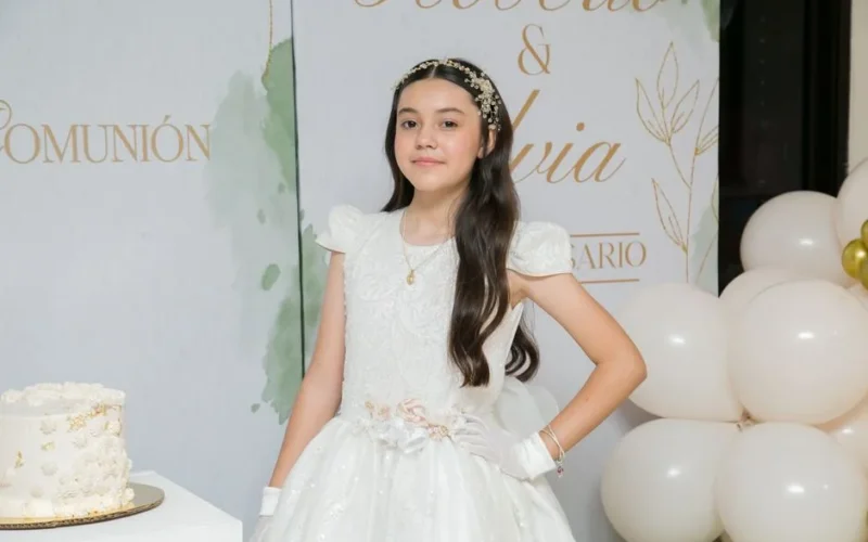 Young girl in elegant First Communion dress with decorations and cake.