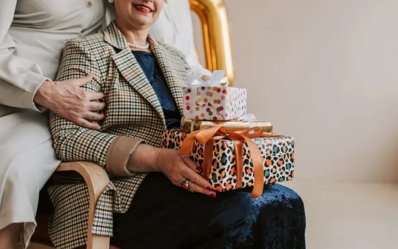 Senior woman receives gifts during indoor celebration with family support.