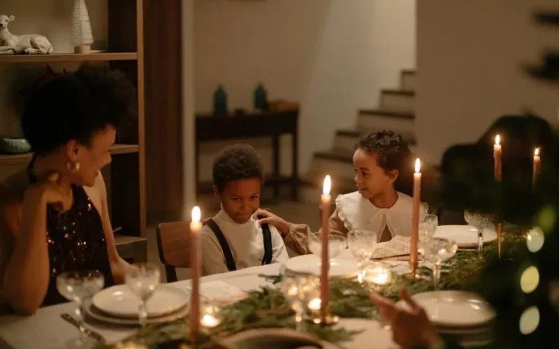 Family gathering around a decorated dining table with lighted candles for a Christmas celebration.