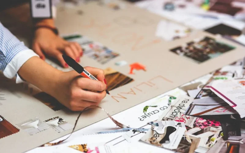 Close-up of a person writing and crafting at a cluttered desk workspace.
