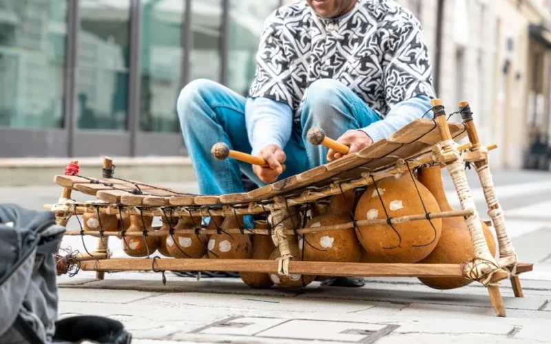 A street musician playing a traditional African balafon in an urban setting.