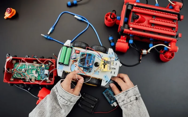 Young hands working on a robotics project with toy cars and circuits, focusing on innovation and education.