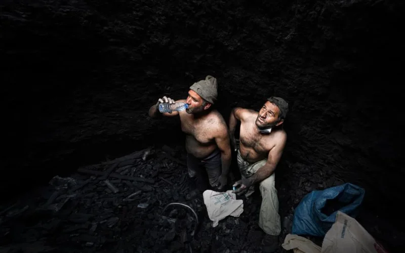 Two shirtless miners taking a break in a dark coal mine in Iran.
