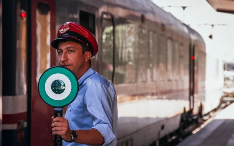 A train conductor at a station holding a signal for train departure.