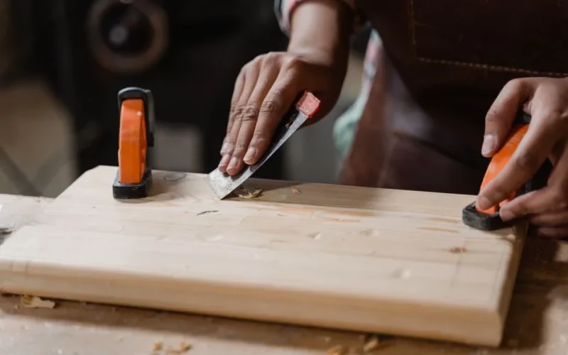 Hands crafting a wooden plank with clamps and tools. A focus on precision woodworking.