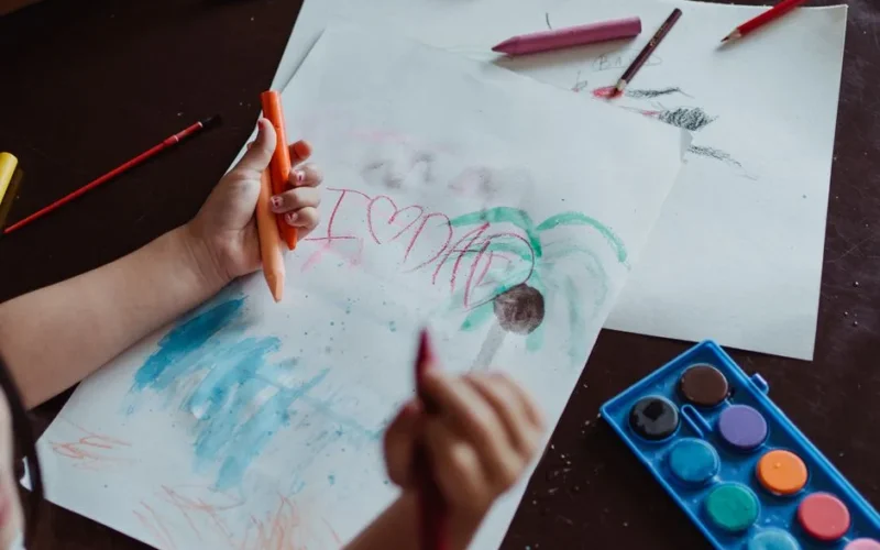 A child drawing with crayons and paints, expressing creativity and love for dad.
