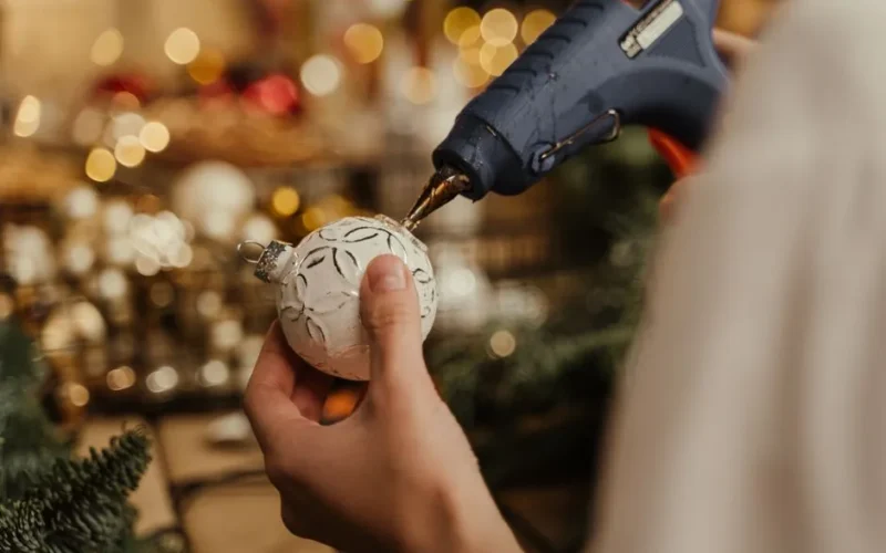 Close-up of hands using a glue gun to decorate a Christmas ornament. DIY holiday craft.