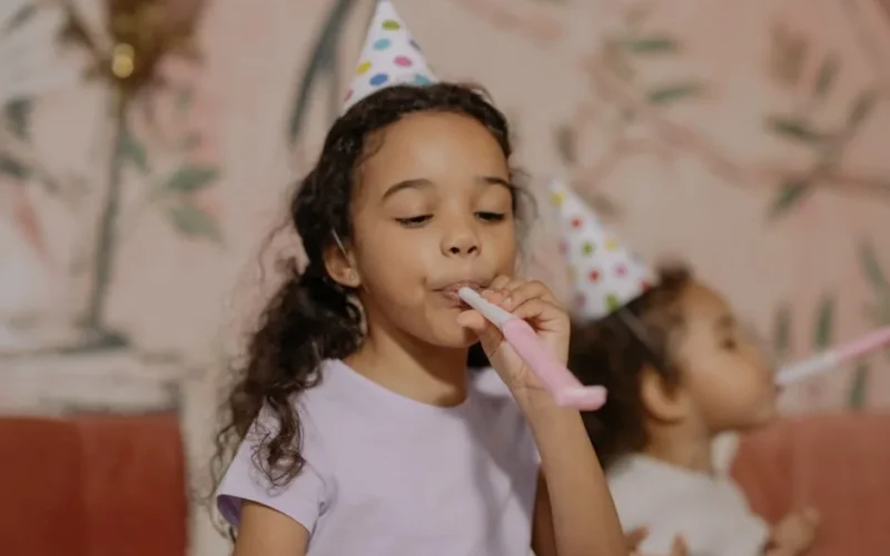 Two young girls in party hats enjoying a birthday party indoors.