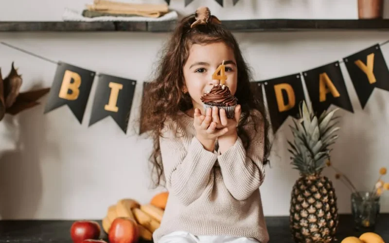 A joyful child celebrates her fourth birthday with a chocolate cupcake indoors.
