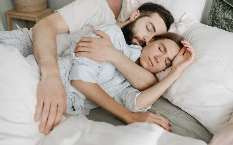 A loving couple embraces warmly in a cozy bedroom setting.