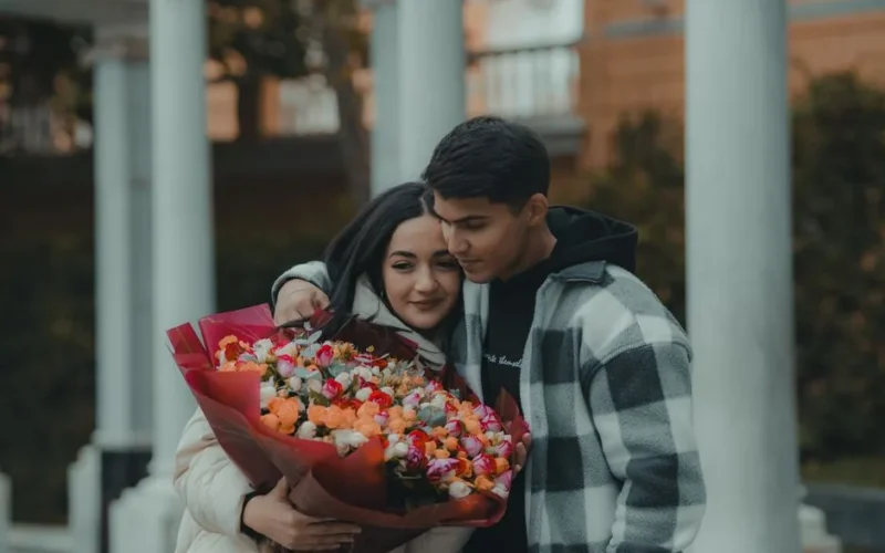 A couple shares a tender embrace holding a vibrant bouquet of flowers, symbolizing love and affection.