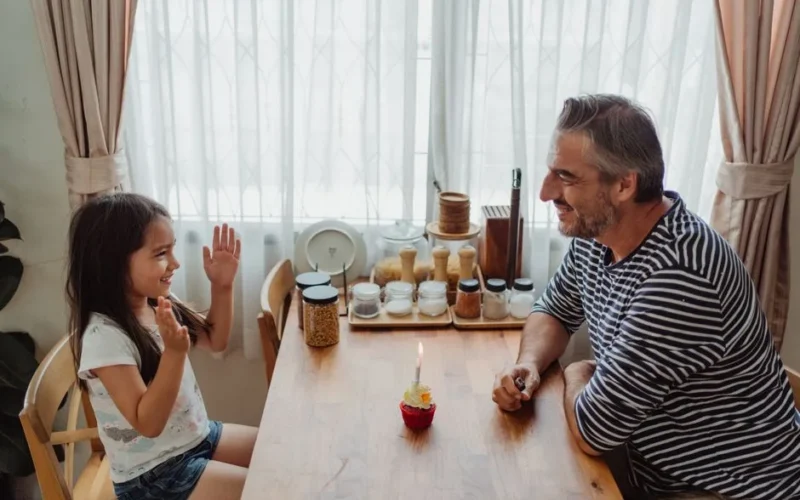 Father and daughter celebrating with a cupcake on a joyful day indoors.