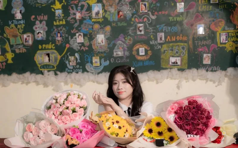 A woman sits in a decorated classroom with diverse floral bouquets on the desk.