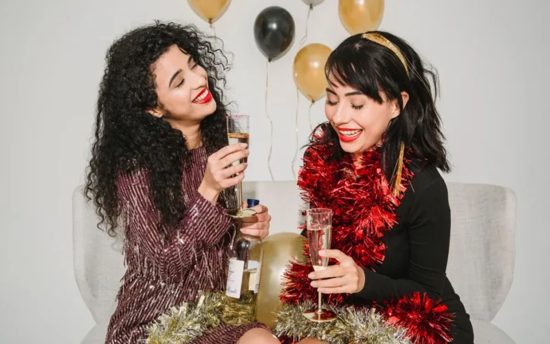 Happy women with bright red lips in shimmering tinsel having fun while celebrating New Year and making wish