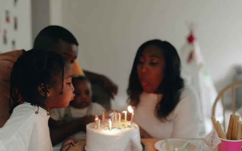 A joyful family celebrating a birthday by blowing out candles on a cake indoors.