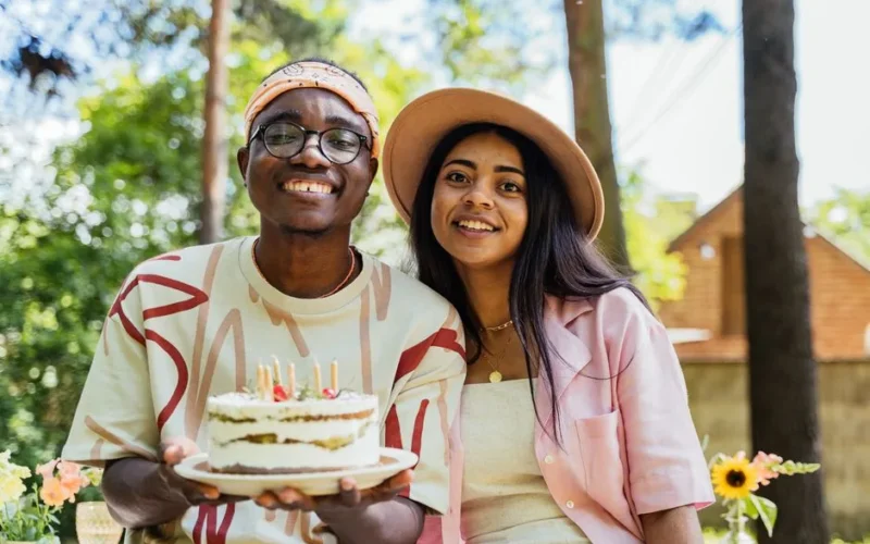 Two adults celebrating a birthday outdoors with a cake adorned with candles, smiling and happy.