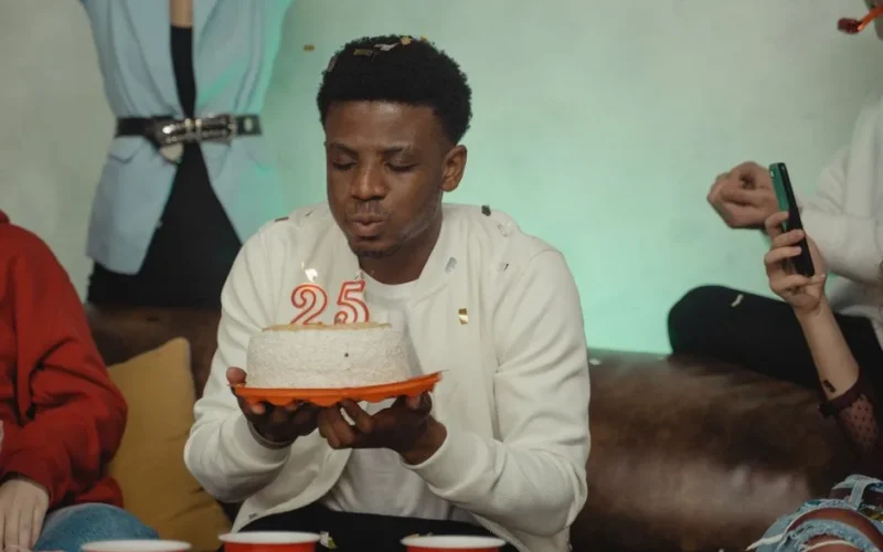 A young adult man blowing out candles on a birthday cake at a party.