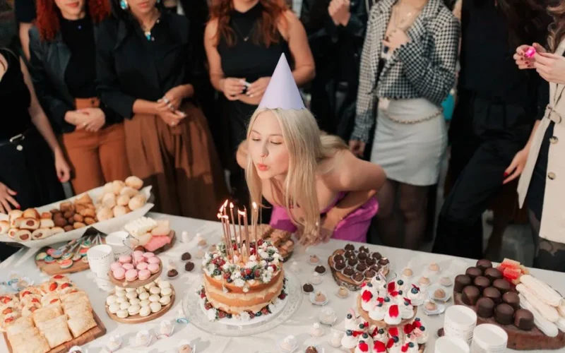 A cheerful young woman celebrates her birthday, surrounded by friends and a variety of delicious cakes and desserts.