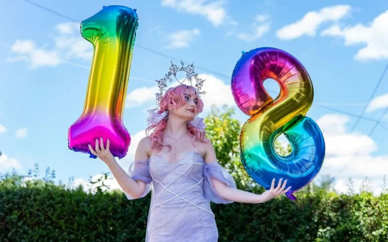 Young woman celebrating her 18th birthday with vibrant number balloons outdoors.