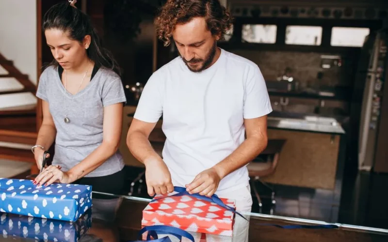 A couple wrapping presents in a modern kitchen setting, depicting teamwork and creativity.