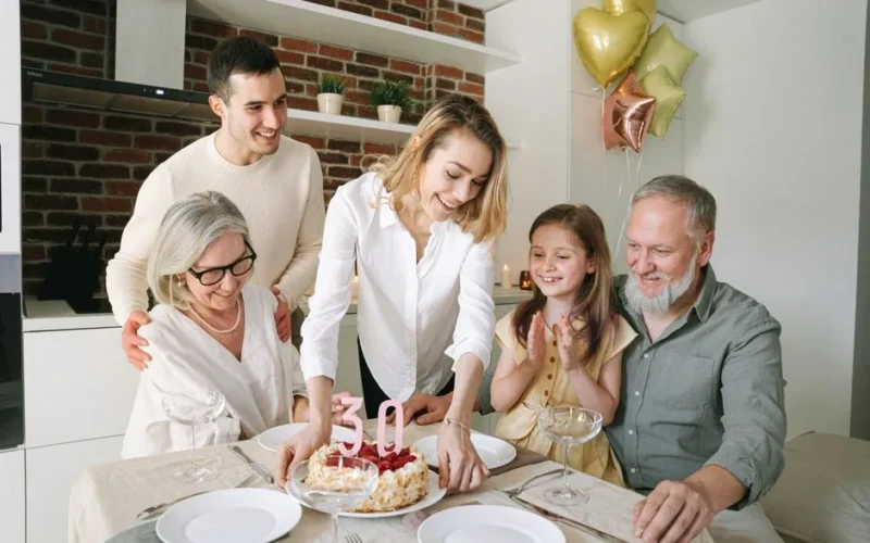 A joyful family gathering around a table celebrating a 30th birthday with a cake and balloons.